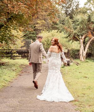 A couple walking through an autumn garden path wearing wedding attire with fall foliage in the background.