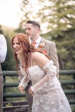 A bride in an elegant lace wedding dress laughs joyfully during an outdoor photoshoot.