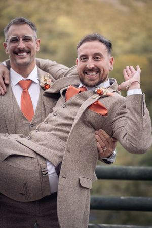 Playful groomsmen in matching tweed suits strike fun pose against mountain backdrop.