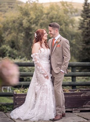 A romantic moment between newlyweds sitting on a rustic wooden bench with fall foliage in the background.