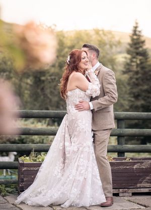Romantic outdoor wedding photoshoot on wooden deck with pine trees in background.