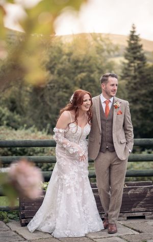 Romantic outdoor wedding portrait of couple standing on wooden deck with mountain scenery and evergreens in background.