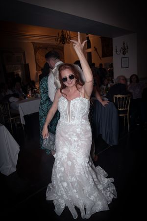 A figure in a white lace wedding dress dances energetically at a wedding reception in a dimly lit venue.