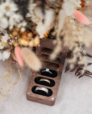 Wedding rings displayed in dark jewelry boxes with soft focus floral decorations.