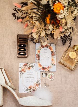 Wedding invitation suite with floral details, perfume bottle and bridal accessories on beige linen.