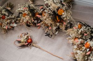 Rustic dried floral arrangements with orange and white flowers laying on a light wooden floor.