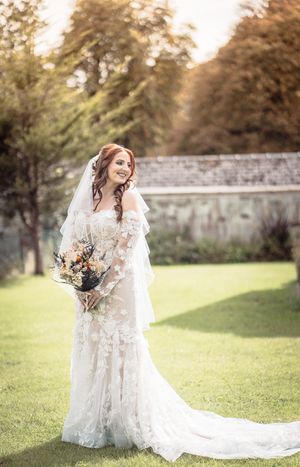 A bride in a flowing lace wedding gown laughs joyfully in a sunlit garden setting during her bridal photo session.