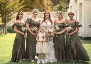 Bridesmaids in olive green dresses gather around bride for outdoor wedding photos.