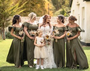Wedding party in olive green dresses poses outdoors in a coordinated line formation.