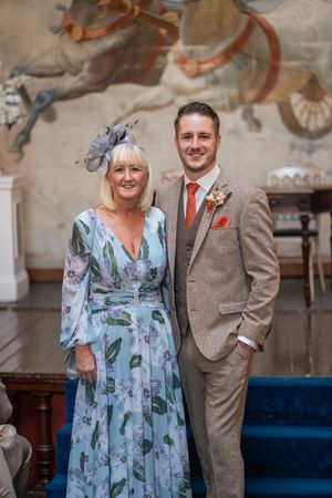Two wedding guests in formal attire standing in front of a decorated wall.