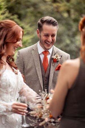 Wedding party in formal attire with grey suits and coral ties sharing joyful moments outdoors.