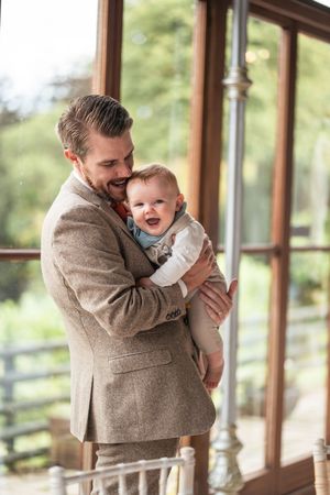 Four candid moments of parent playing with and kissing a laughing baby in a brown suit on a sunlit porch.