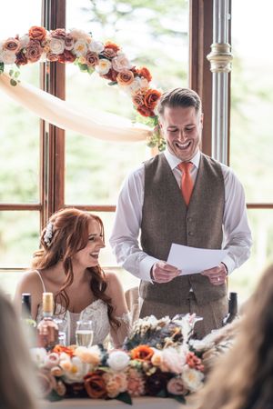 Wedding reception scene with floral centerpieces and joyful table interactions.