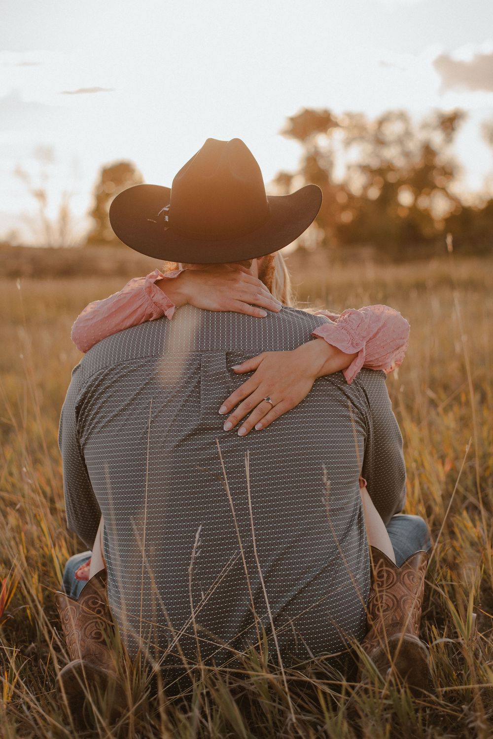 Couple sitting together in tall grass during sunset with cowboy hat.