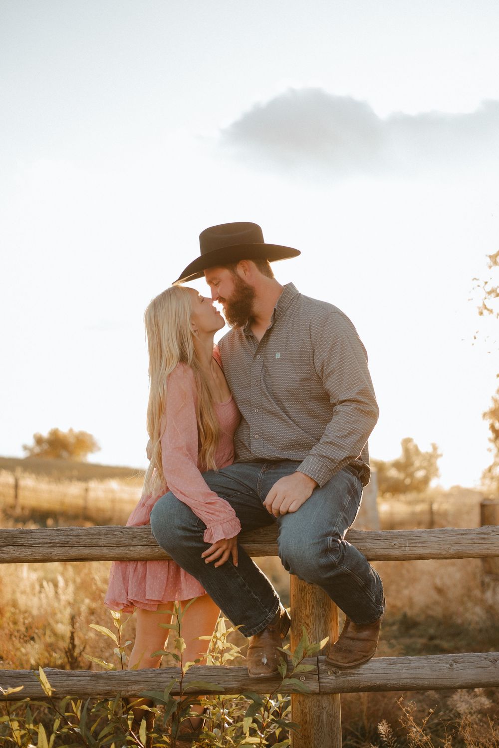 Couple sitting on wooden fence during golden hour sunset.