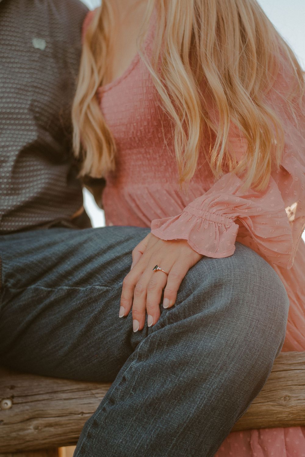 Detail shot of couple sitting on rustic wooden fence during engagement session.