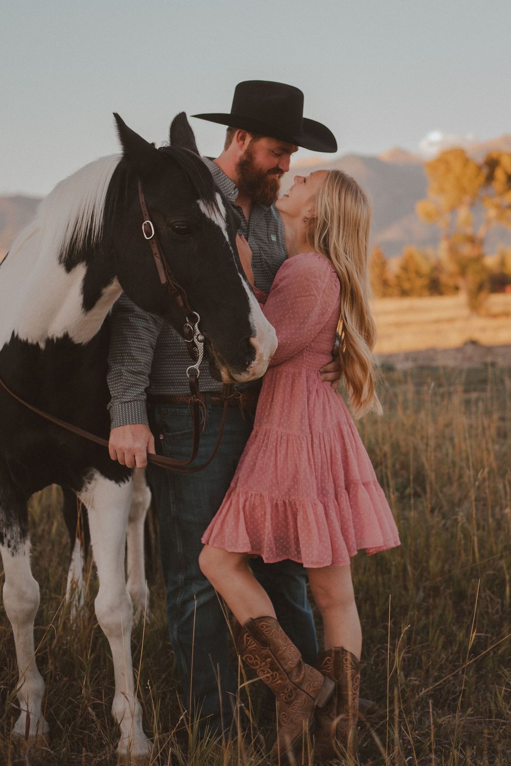 A couple poses with their black and white horse in a rustic field during golden hour.
