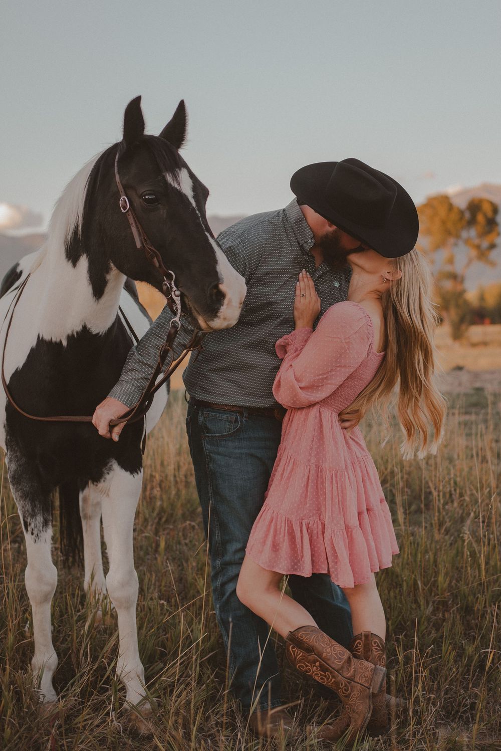 A romantic country photoshoot featuring a couple and their paint horse in a golden field.