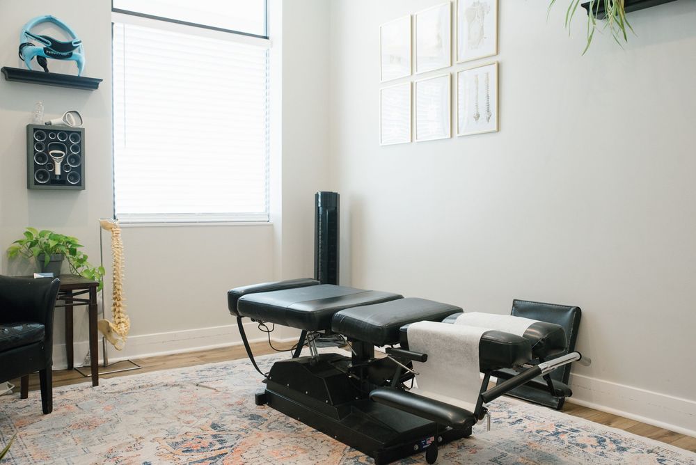 Clean chiropractic adjustment table in bright treatment room with decorative rug and plants.
