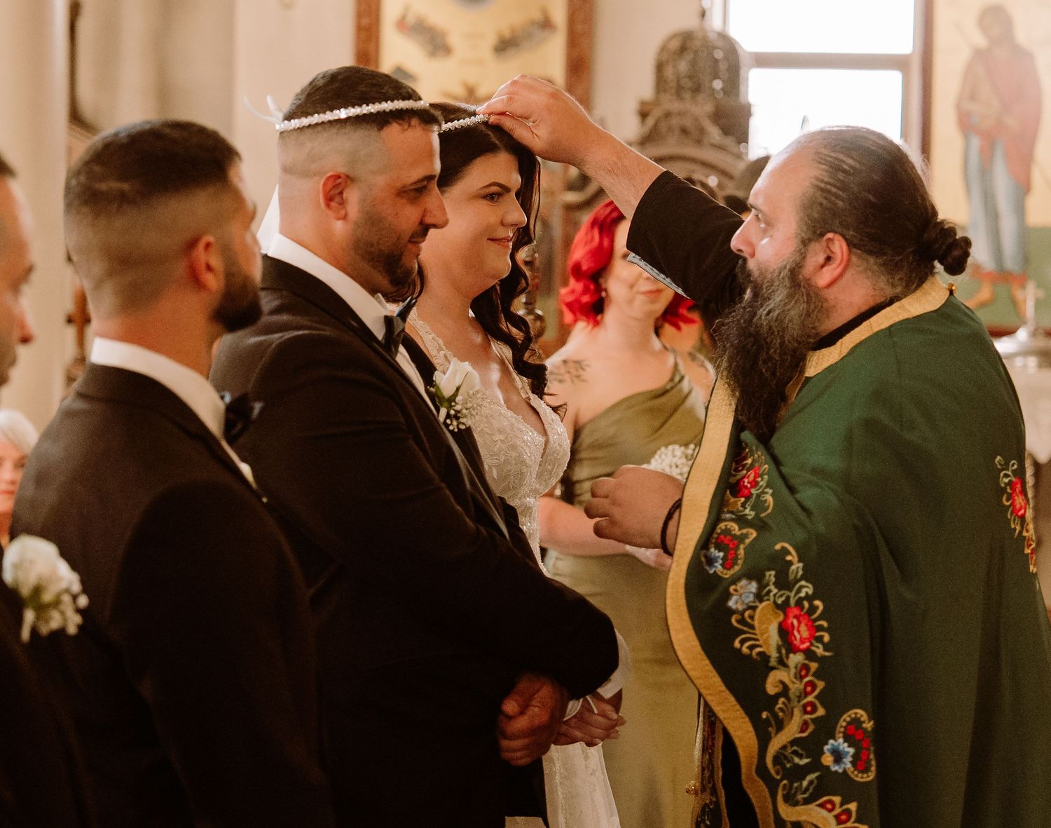 A groomsman in a dark suit and hat stands at attention during a formal wedding ceremony.