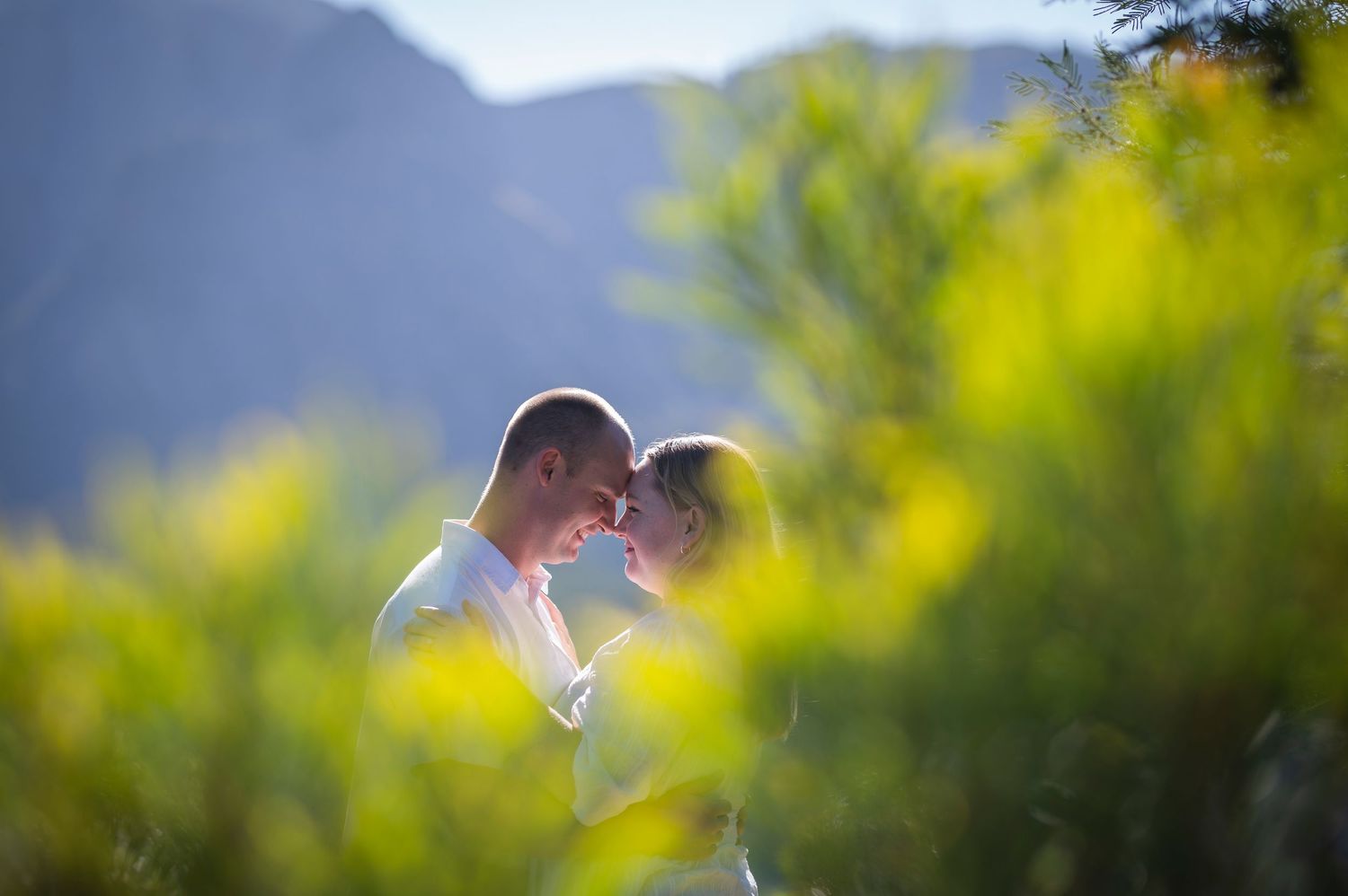 Romantic silhouettes embrace in joyful moment surrounded by vibrant yellow and green bokeh lighting effects in nature.