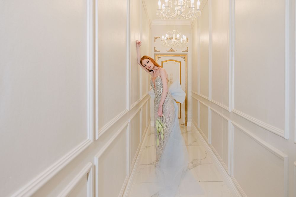 A long, elegant white hallway with crystal chandeliers and decorative wall moldings creates a luxurious perspective.
