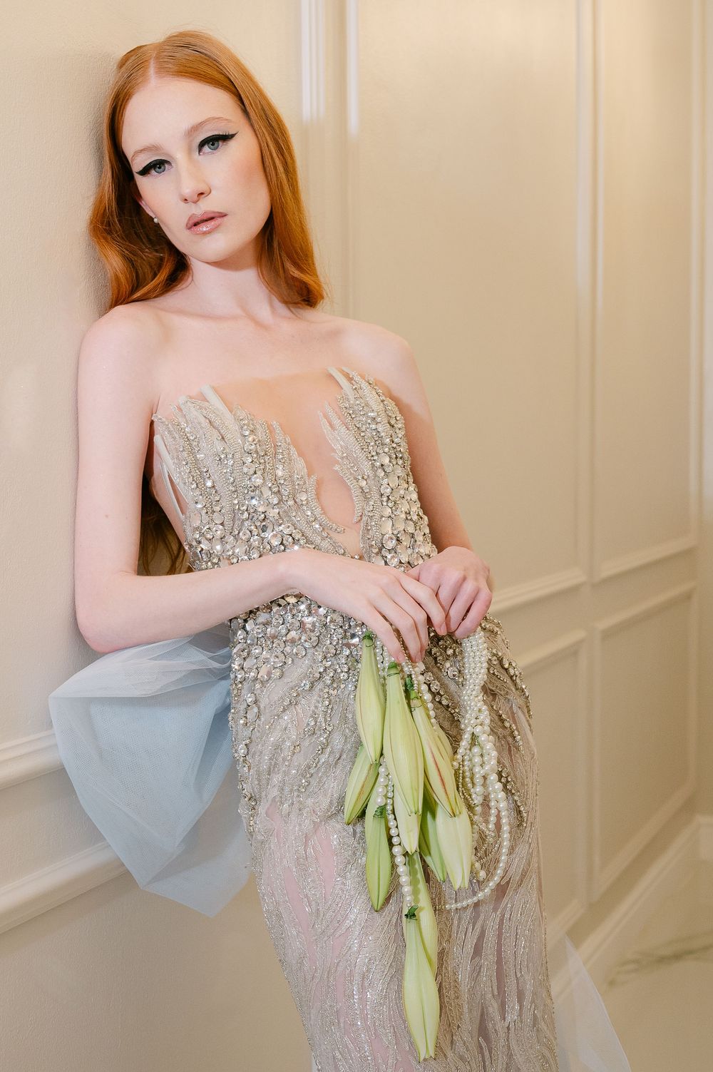 An elegant sparkly sequined evening gown in silver with a green bow accent is displayed in a luxurious room setting.