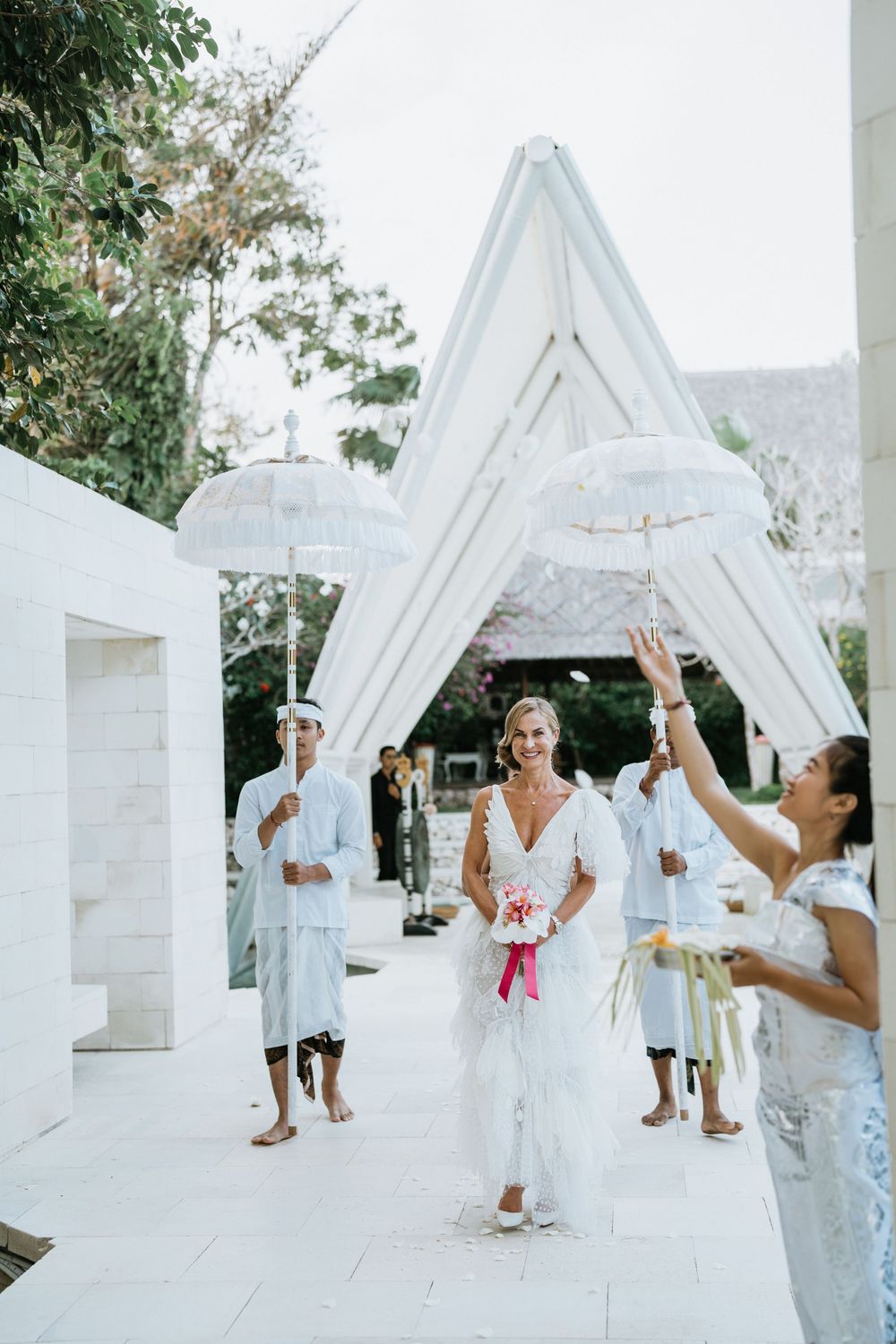 Wedding celebration in a white architectural structure with decorative parasols and elegant attire.
