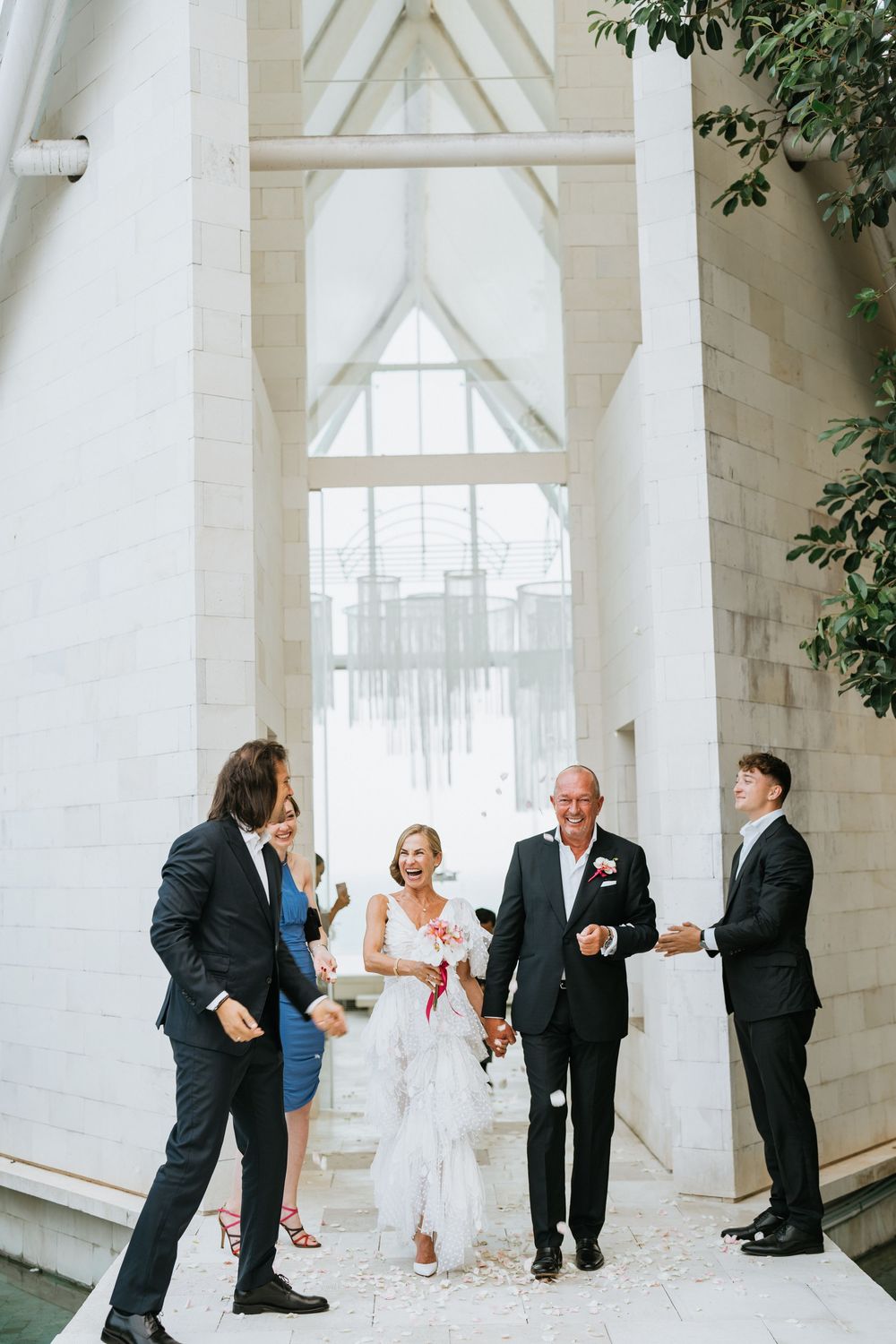 Wedding party exits through a modern white chapel archway in formal attire.