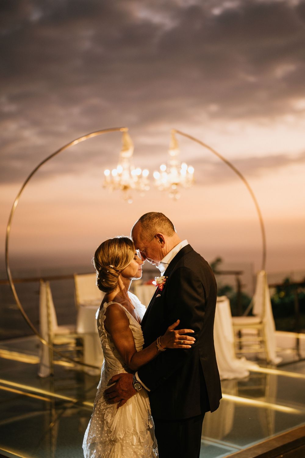 Romantic sunset moment under golden arch with chandeliers at outdoor reception.