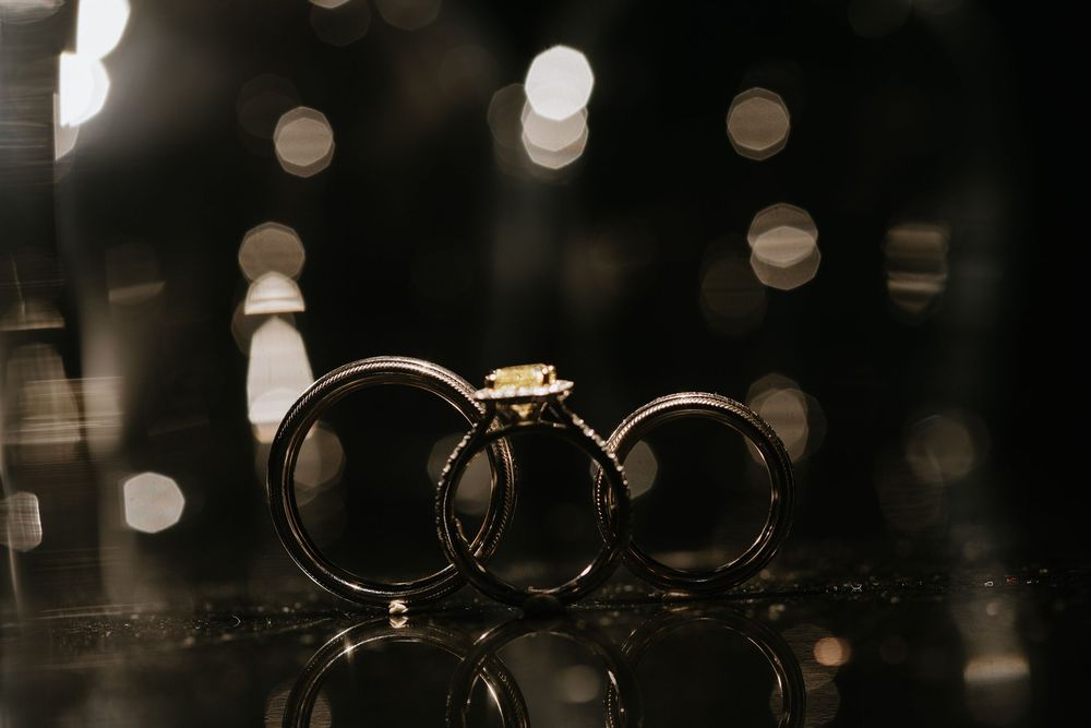 Artistic macro shot of wedding rings with bokeh lights in dark background.
