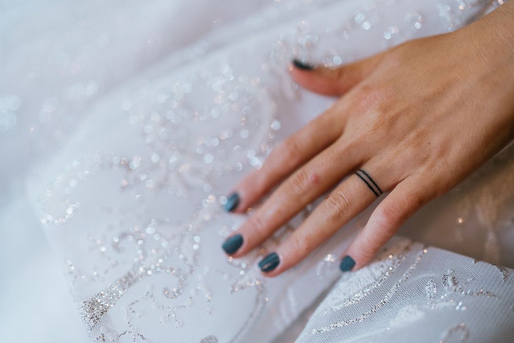 Close-up of hands with blue nail polish touching intricate beadwork on a white wedding dress.