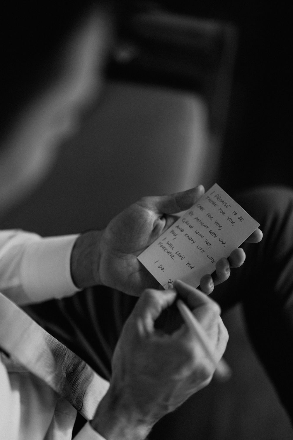 Hands holding handwritten wedding vows or letter in dramatic black and white lighting.