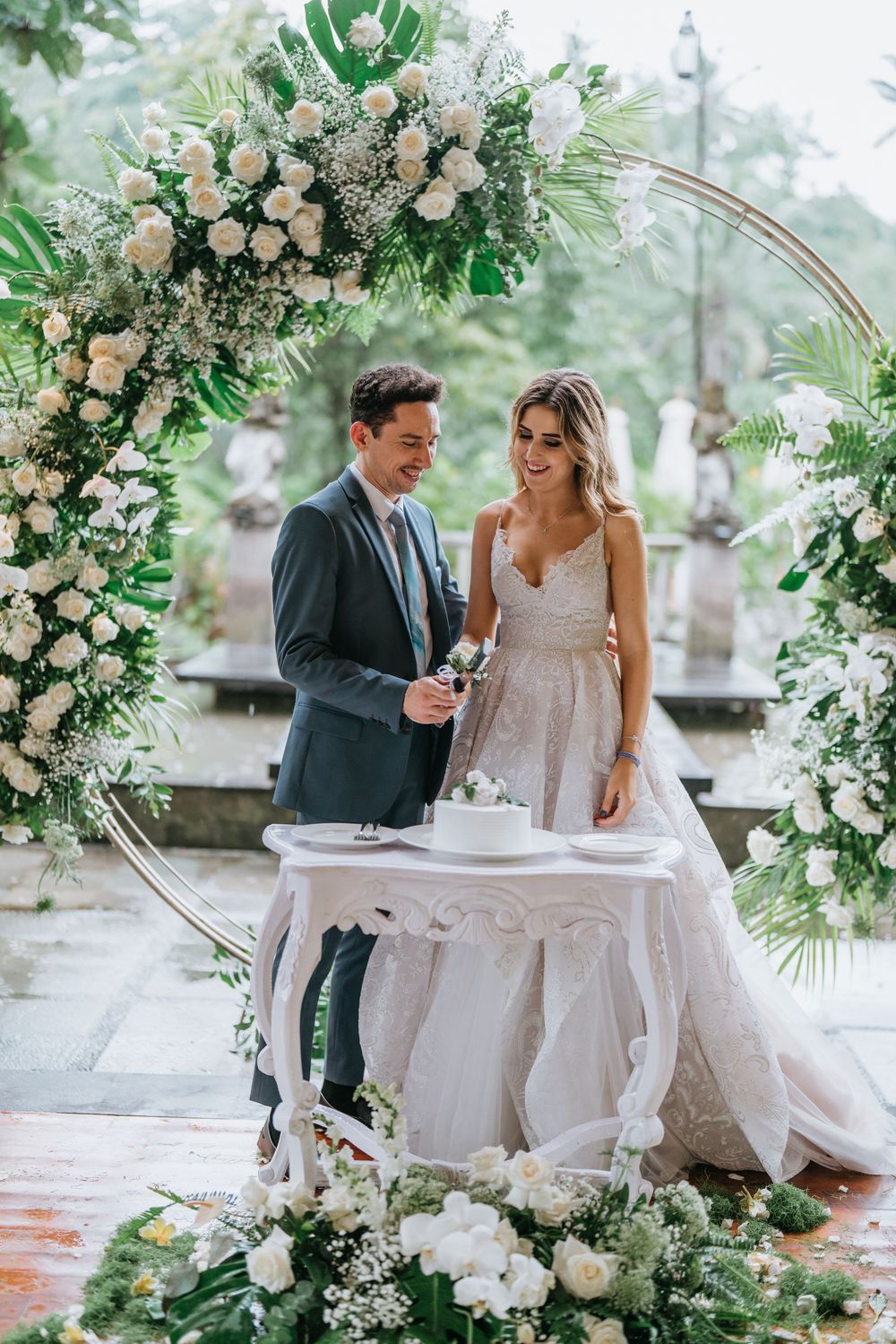Elegant wedding setup with a circular floral arch and white roses surrounding a cake table.