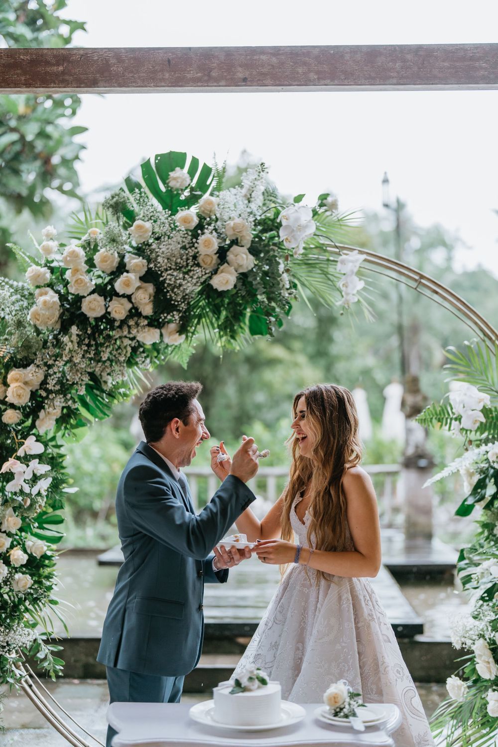 Wedding couple sharing a playful moment during their cake cutting ceremony under a floral arch.