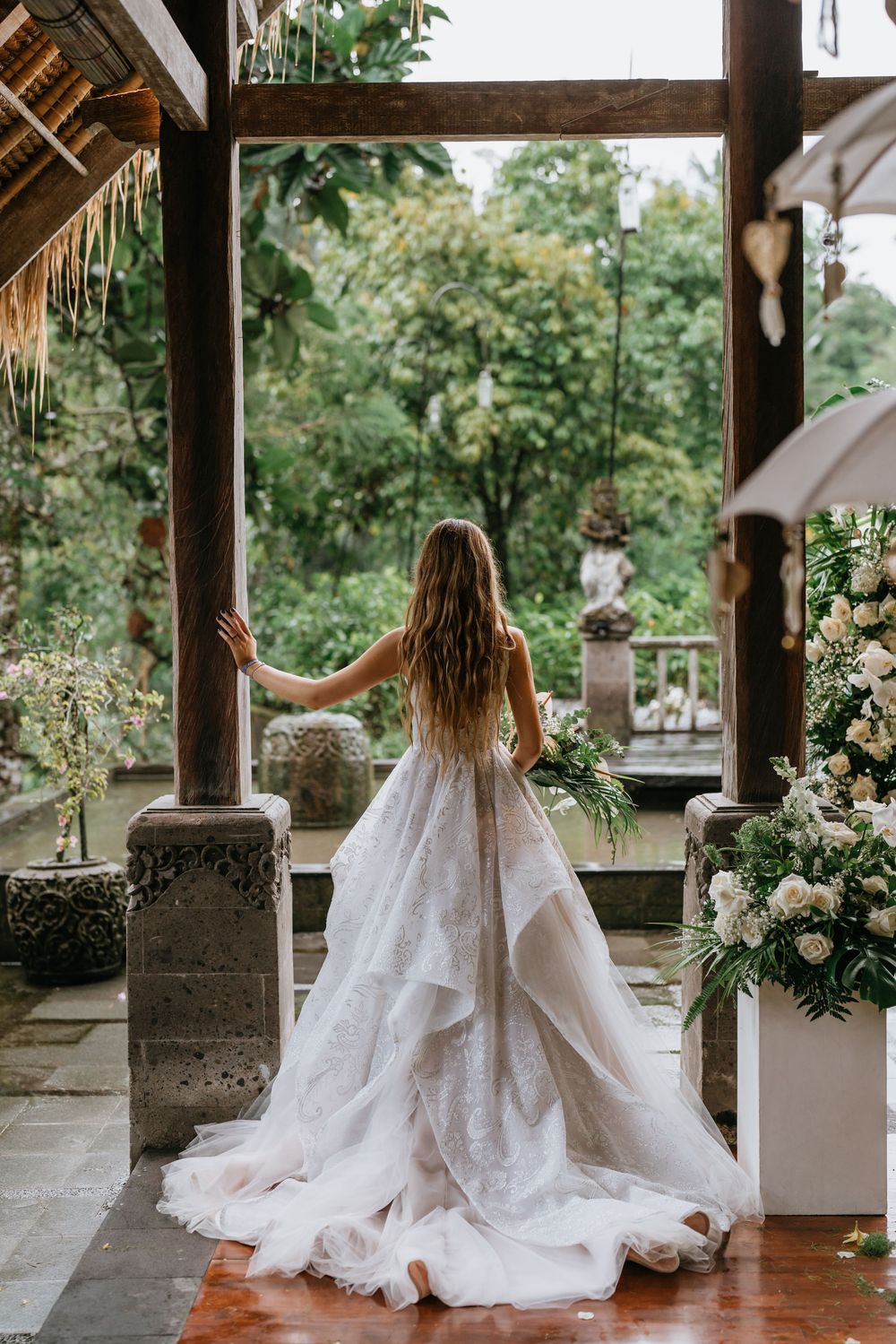 Flowing white wedding dress with long train displayed in a rustic covered porch setting.