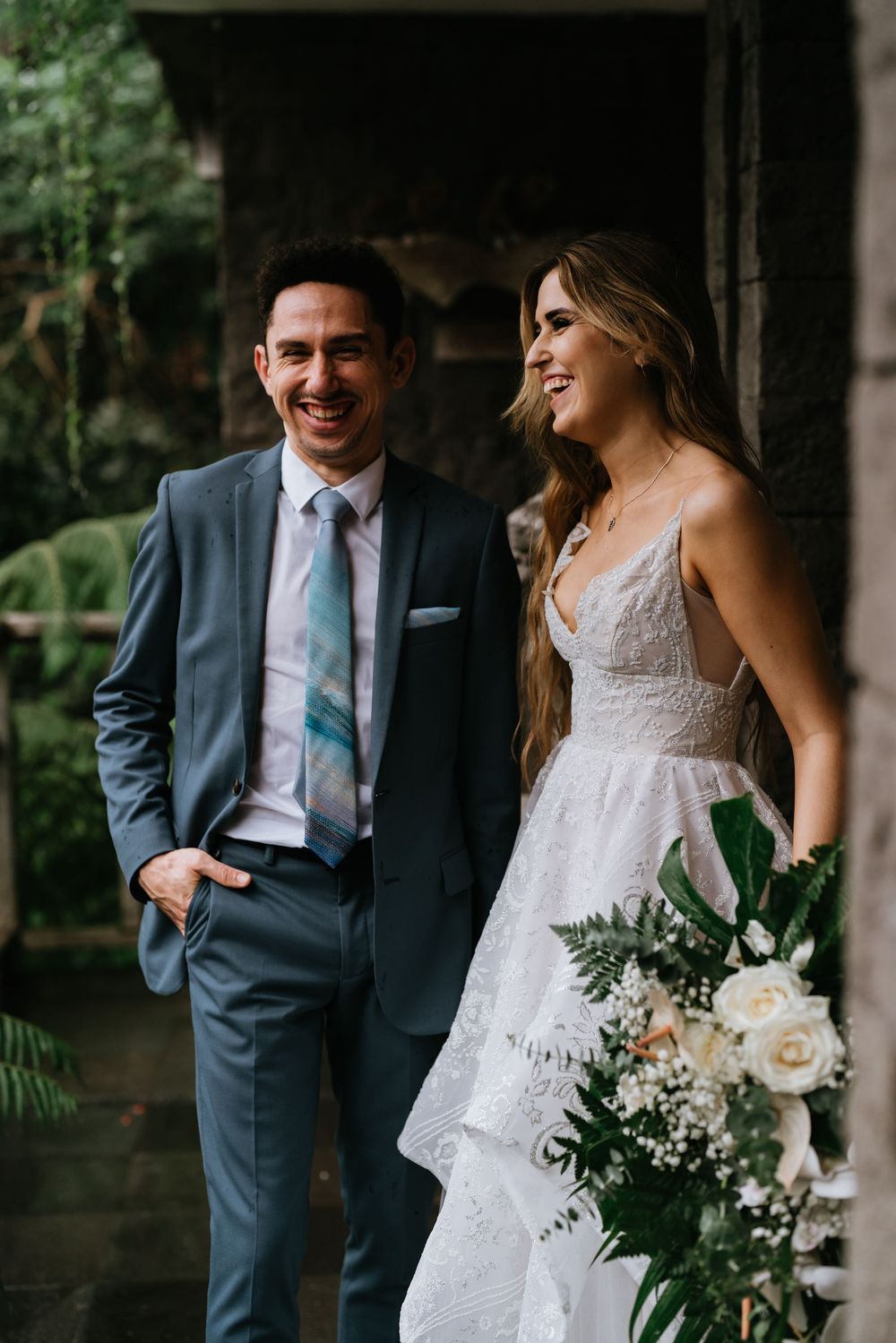Wedding couple shares joyful candid moments in formal attire against dark background.
