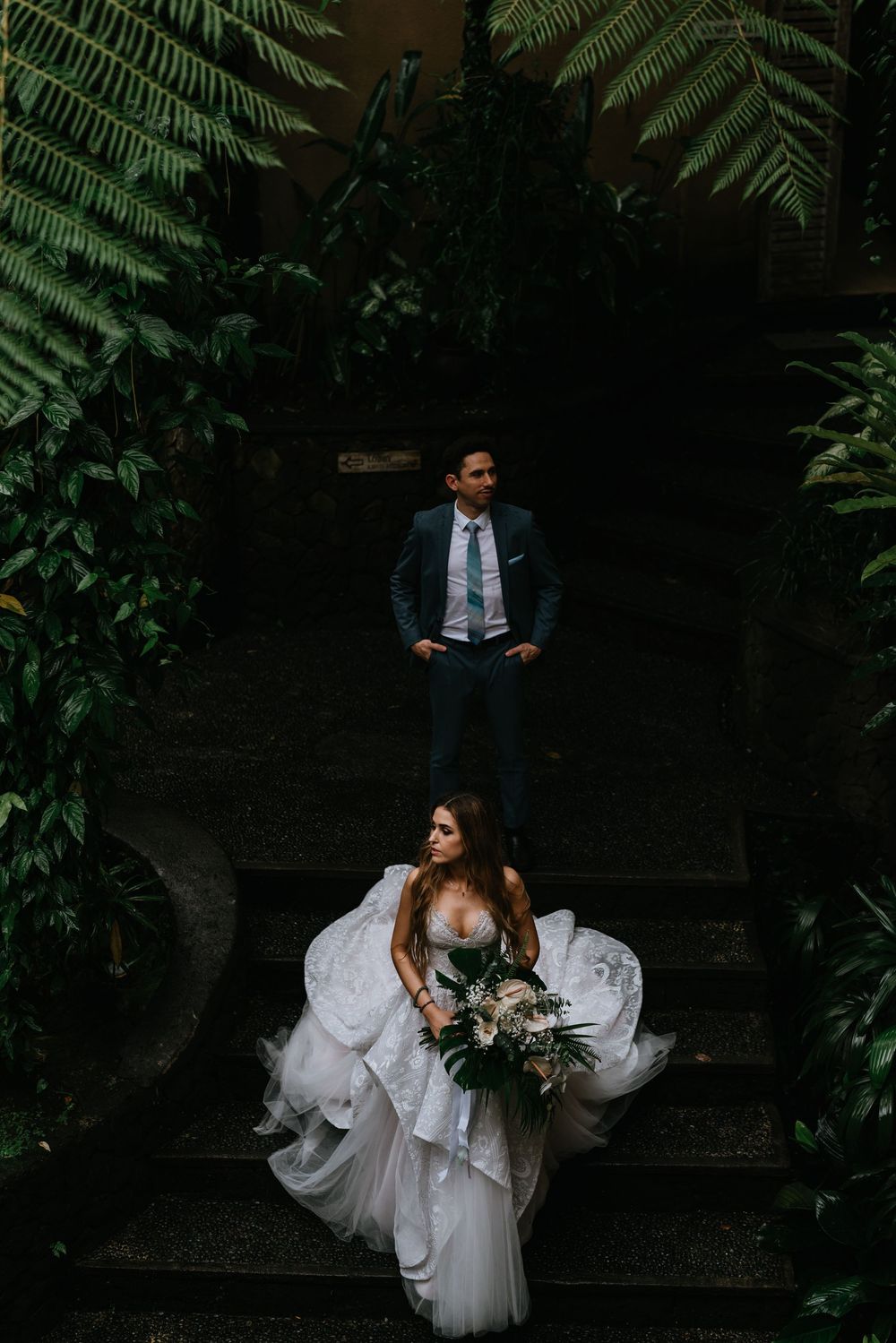 Dramatic wedding portraits taken on wooden steps surrounded by lush ferns and greenery.