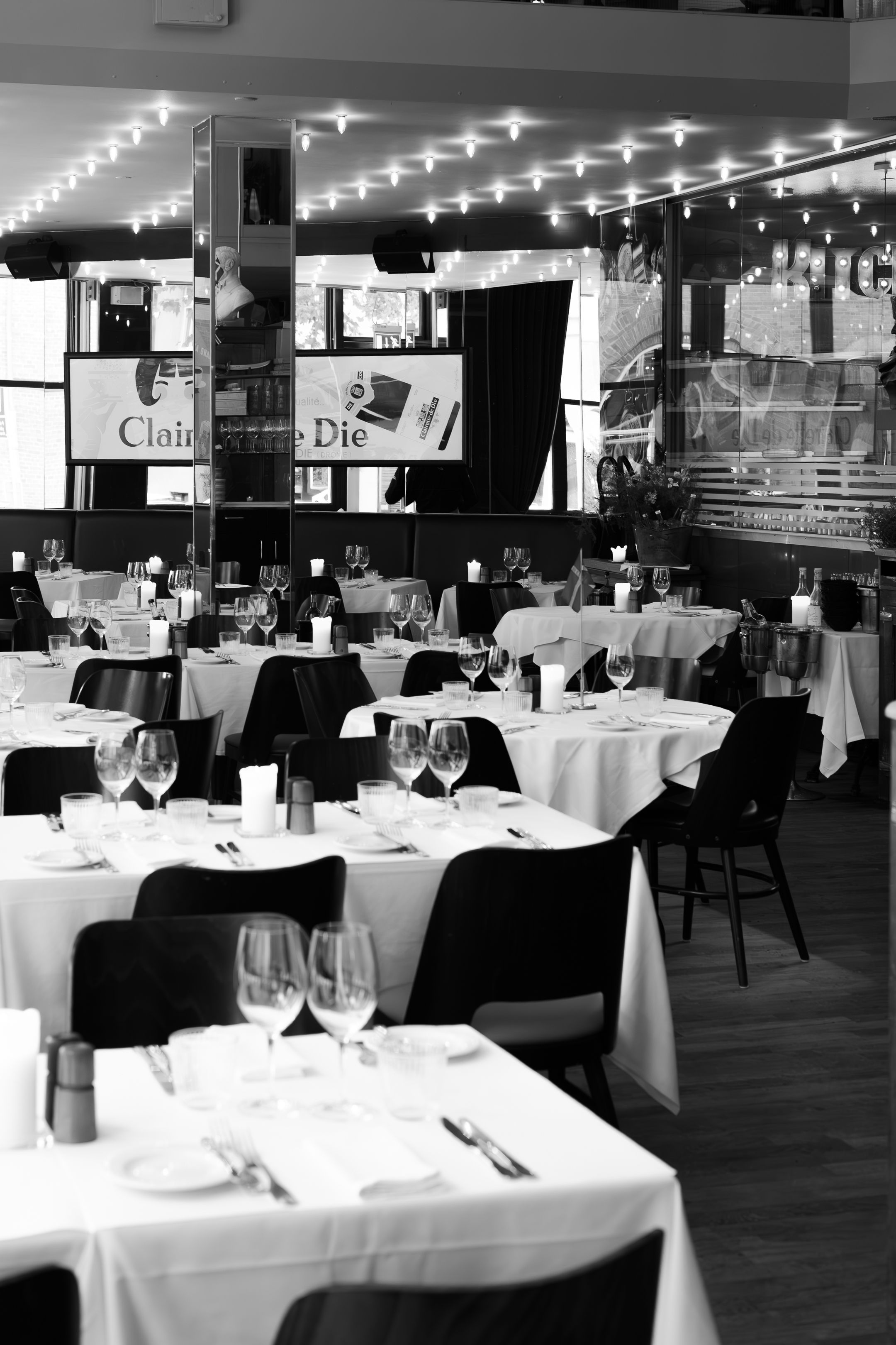 Black and white photo of an elegant restaurant interior with white tablecloths and string lights creating an intimate ambiance.