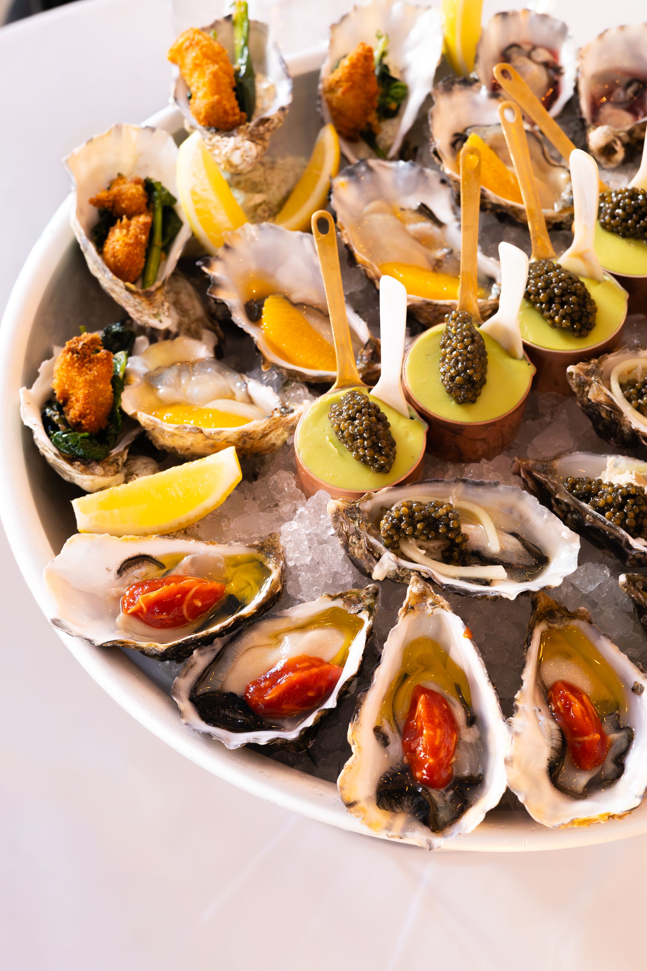 Fresh oysters garnished with caviar and lemon slices served on ice in white plates.