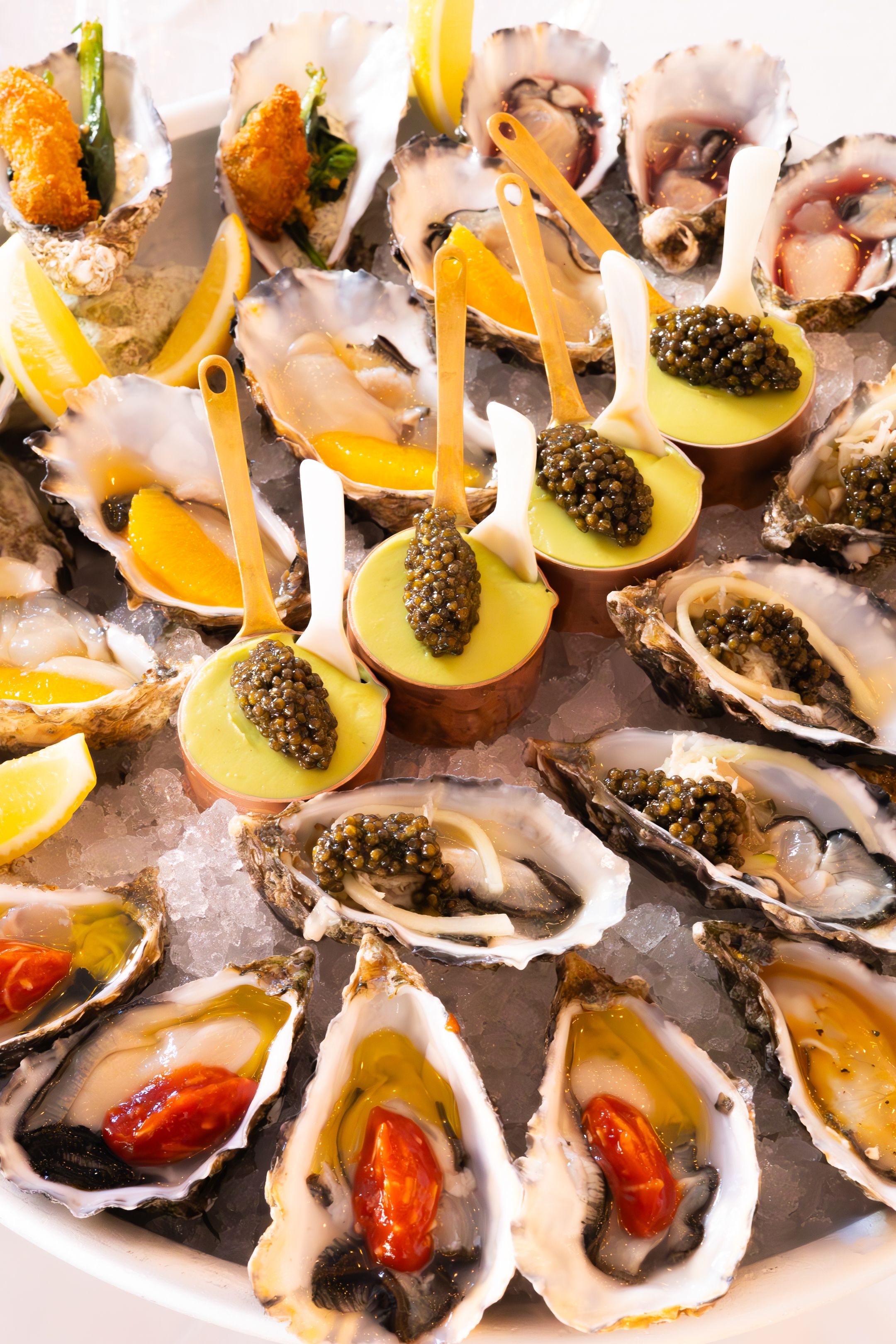 Fresh oysters on the half shell garnished with caviar, lemon wedges and red sauce arranged on a serving platter.