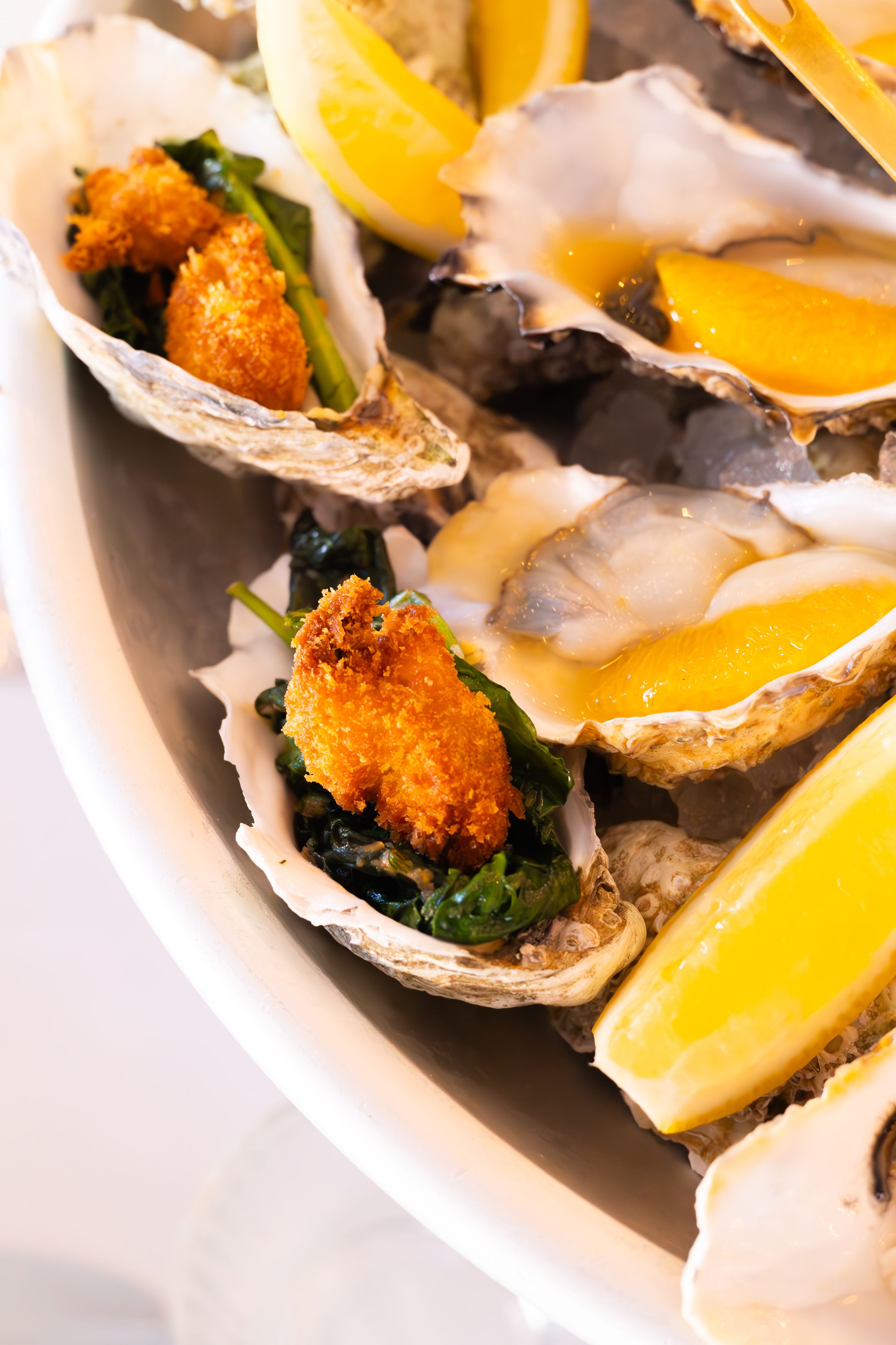 Fresh oysters on the half shell garnished with crispy toppings and served with lemon wedges on a white plate.