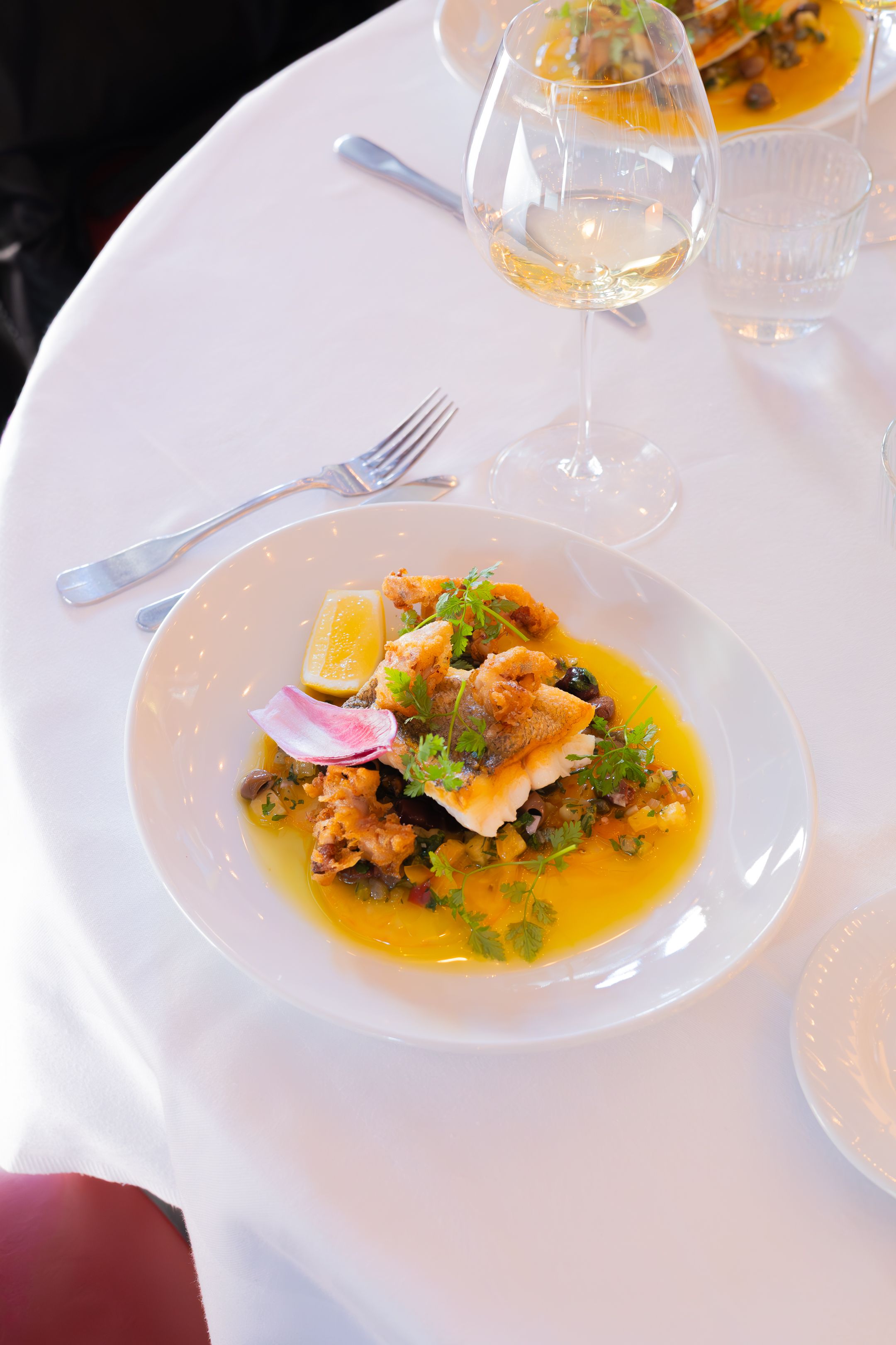 Elegant plated fish dish with orange sauce and microgreens served on white china in an upscale restaurant setting.