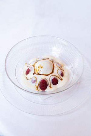 Elegant dessert plate with creamy white mousse decorated with raspberry dots and caramel drizzle on a glass dish.