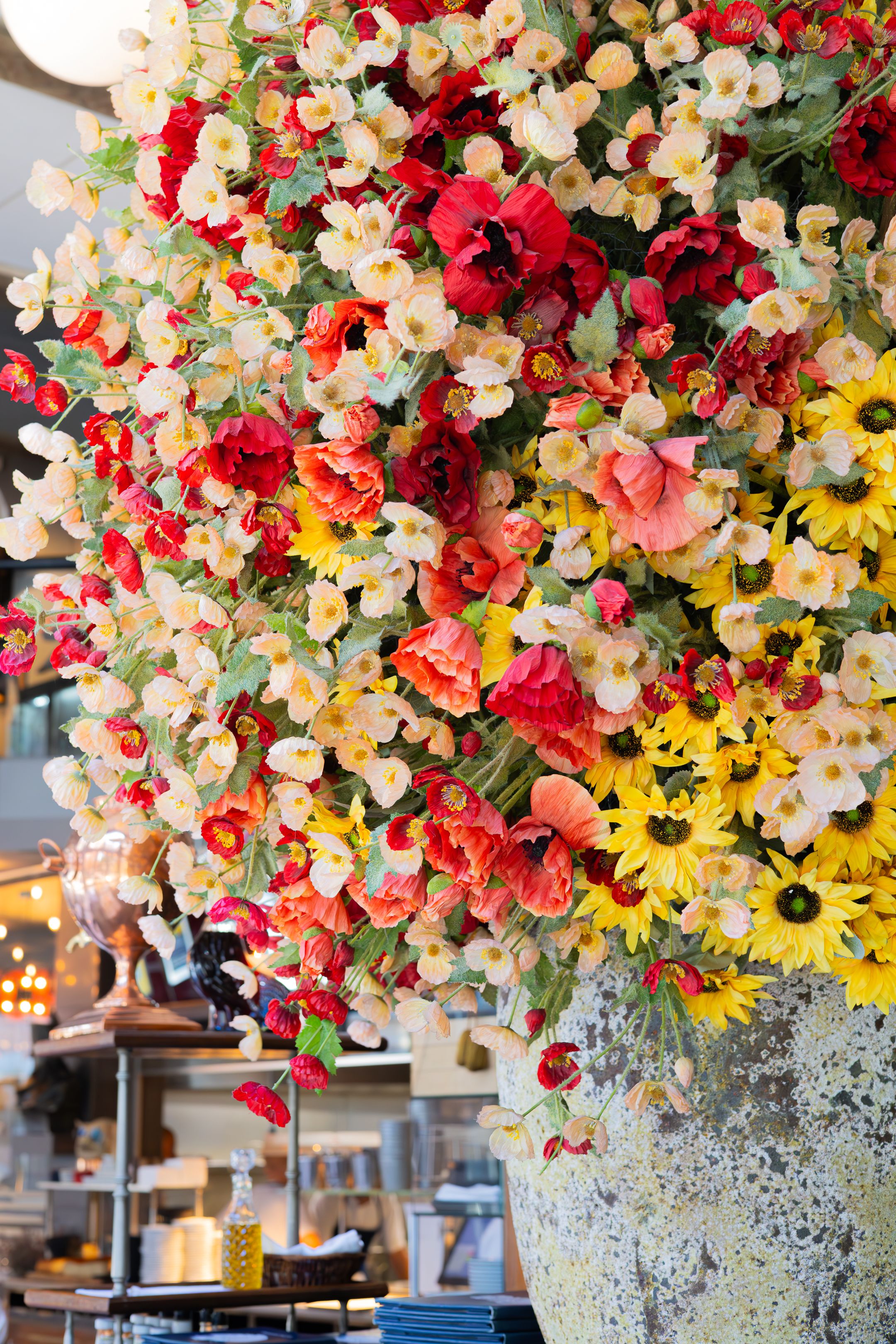 A vibrant floral arrangement with red, yellow, and cream colored flowers cascading from a textured gray vase.