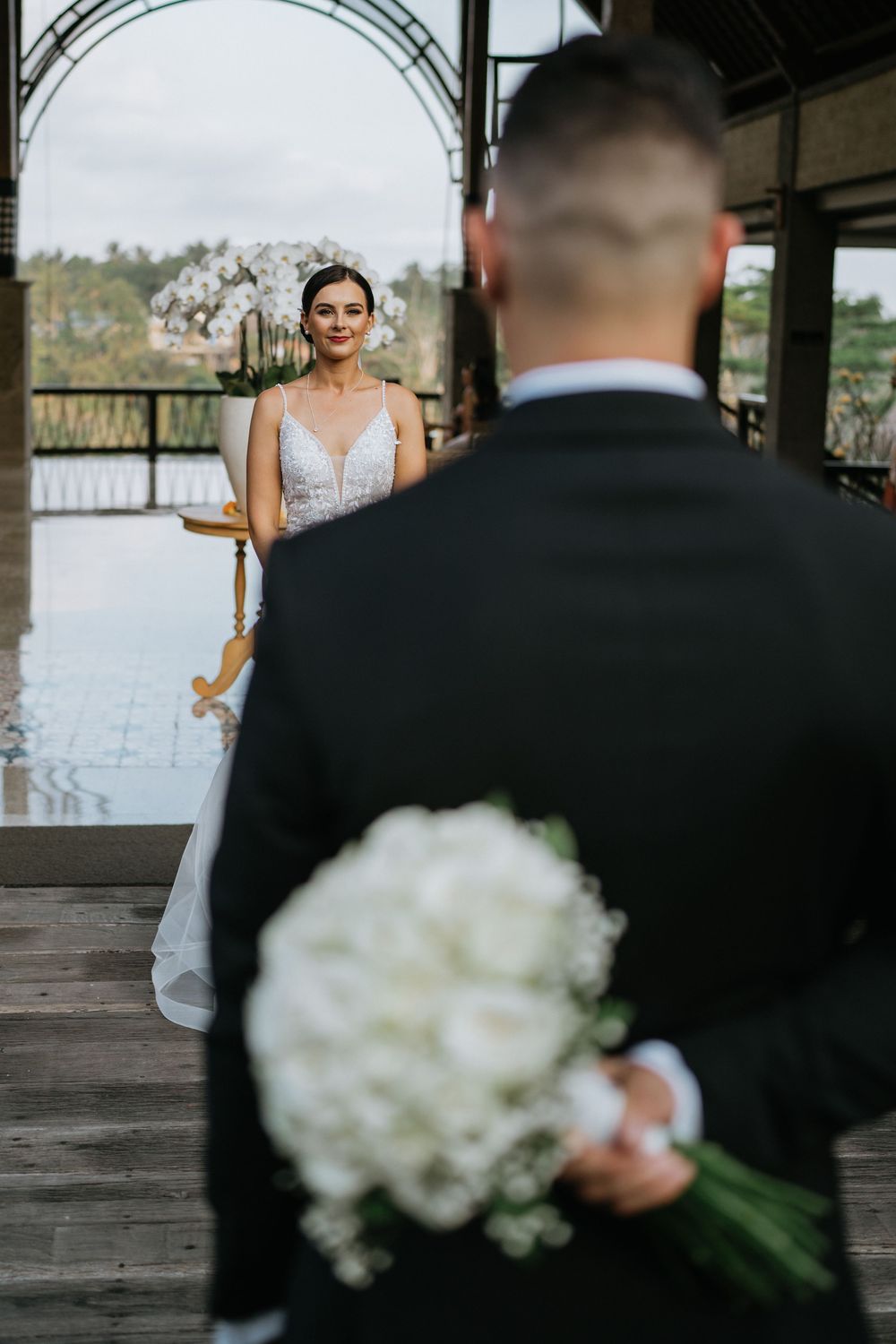 Wedding first look scene with white bouquet and waterfront backdrop.