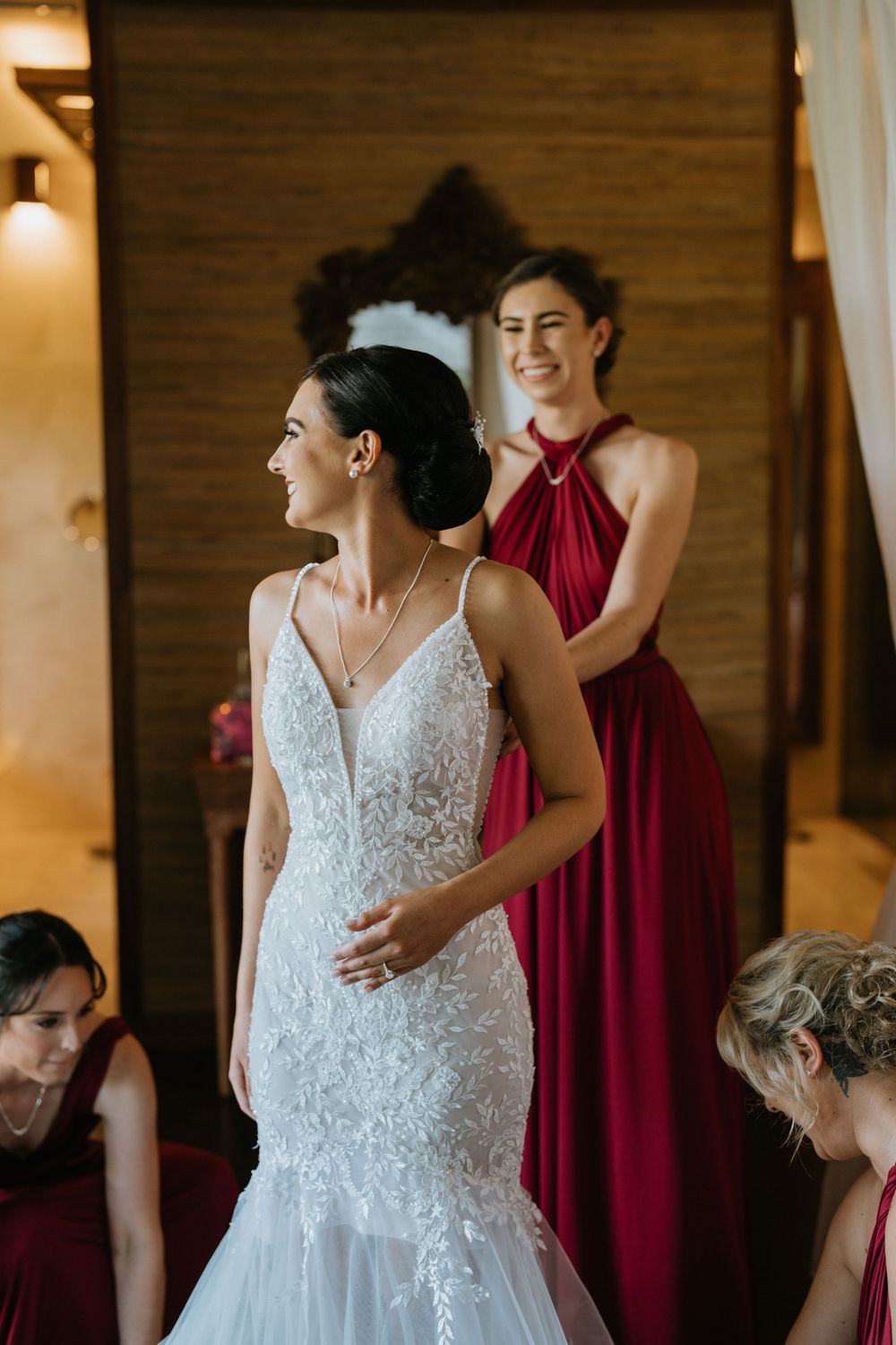 Bride in lace dress shares joyful moments with bridesmaids in burgundy dresses.