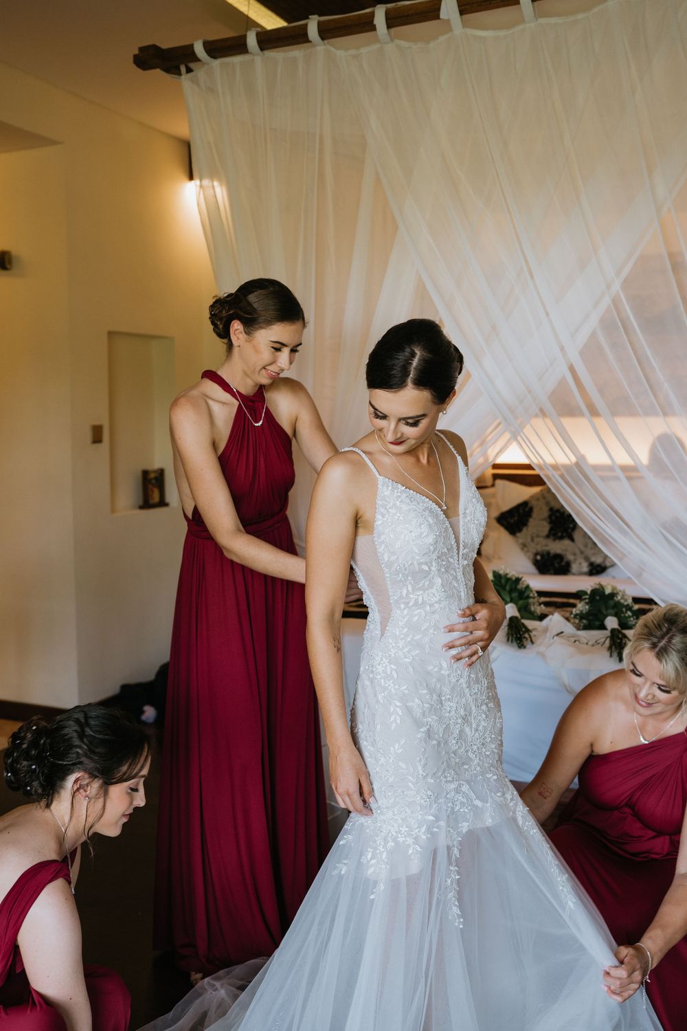 Bridesmaids assist with final wedding dress adjustments before ceremony.
