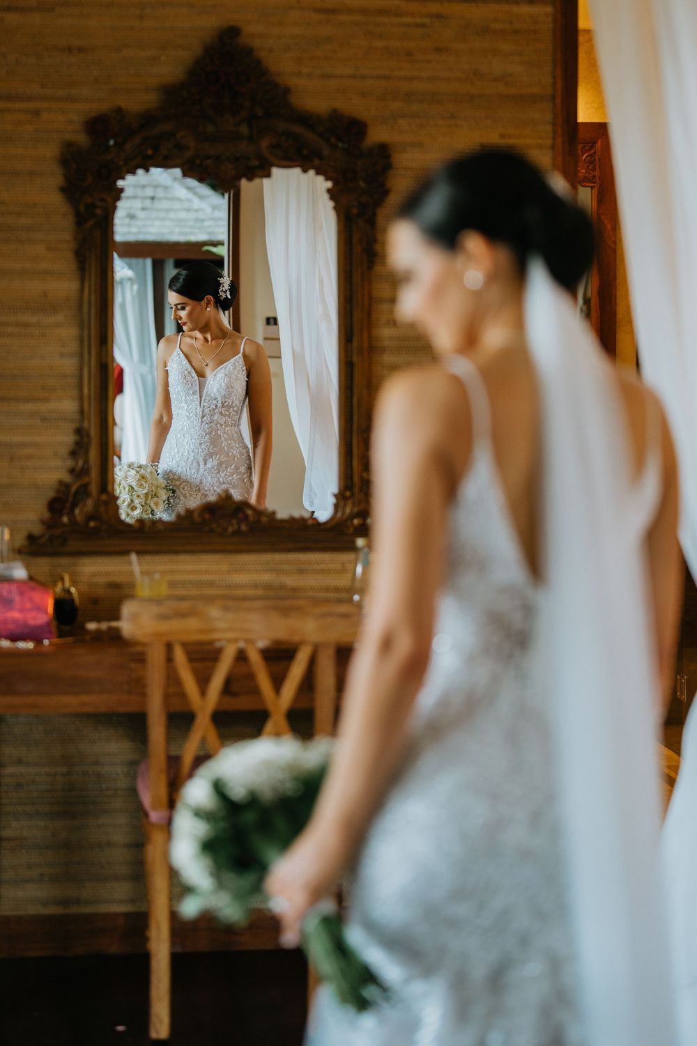 A bride in a white lace dress gets ready in a rustic wooden room with mirrors.