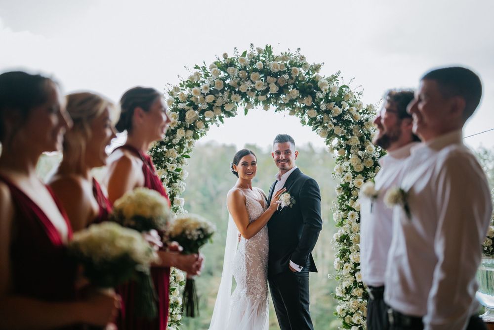 Wedding party celebrates under floral decorations during outdoor ceremony.